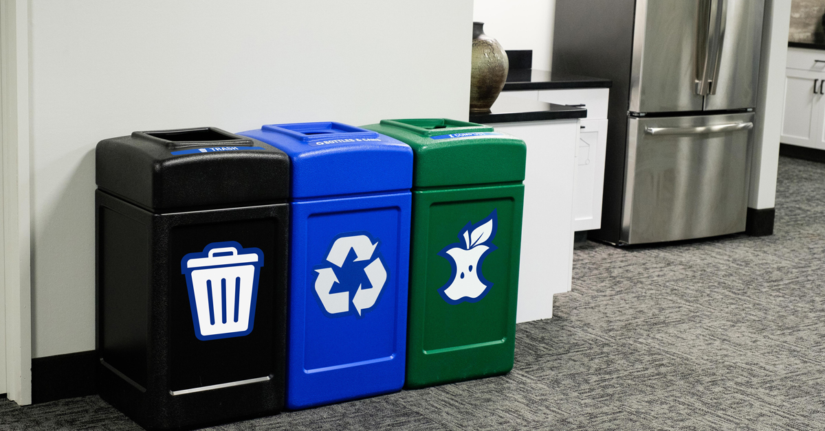 a black trash receptacle, blue recycling receptacle and green compost receptacle in a mult-stream set up inside an office kitchen area